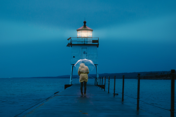 Person med paraply på pir nära fyr i skymning