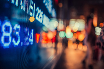 Börsskärm i stadsmiljö med ljusa siffror och suddiga silhuetter av människor