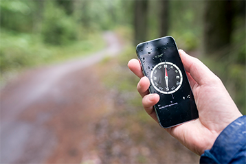 Person håller en smartphone med en kompassapp öppen i skogen