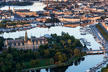 Flygfoto över Stockholm med Nordiska museet i förgrunden och stadens silhuett samt vatten i bakgrunden