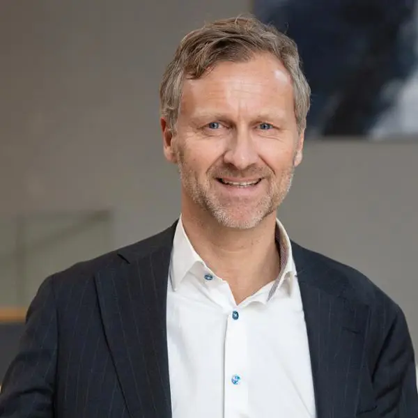 Man i kostym, ler mot kameran i en professionell miljö