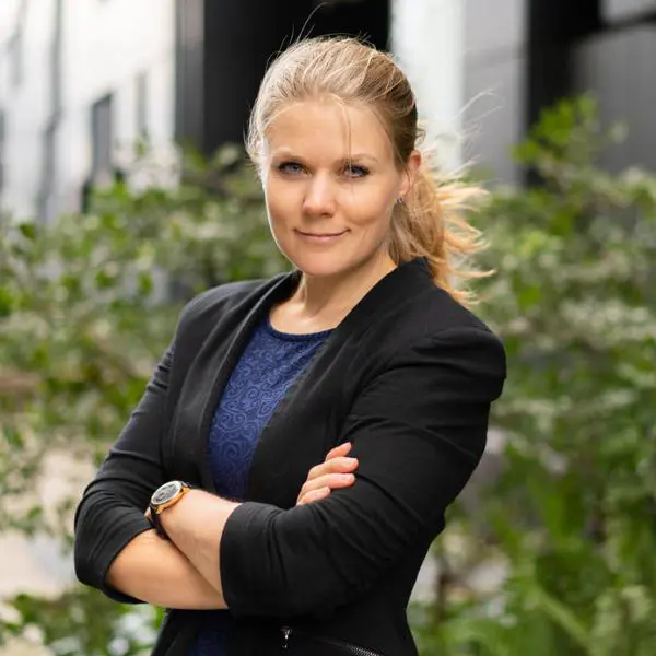 Kvinna i affärskläder står utomhus med armarna i kors, grönska i bakgrunden